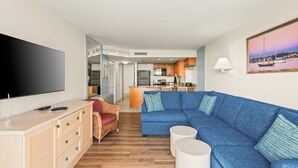 Ett modernt vardagsrum med en blå hörnsoffa, en platt-TV och en matplats med träskåp.