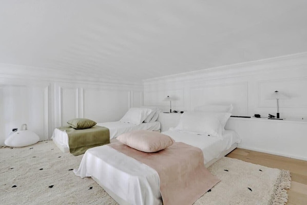 A minimalist bedroom with two beds, a large window, and a white color scheme.