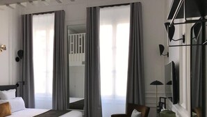 Quarto de hotel com uma cama grande, uma cadeira, uma escrivaninha e um espelho.