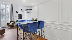Uma sala de jantar moderna com uma mesa comprida e cadeiras azuis, uma televisão na parede e uma janela com cortinas.