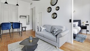 Una sala de estar moderna con un sofá gris, dos sillas azules, una mesa de centro negra y un comedor con una mesa y sillas blancas.