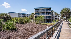 Un hotel de varios pisos con balcones, un muelle de madera y vegetación circundante.