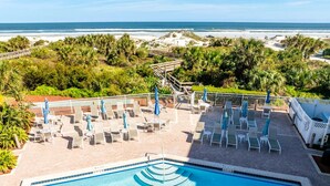 A pool area with lounge chairs and umbrellas, a view of the beach, and a lifeguard stand.