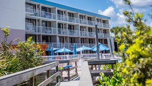 A multi-story hotel with balconies, outdoor seating, and a pool area. - Beach Mode: ON — Garden-Level 1BR Just Steps to the Surf (St. Augustine Beach)