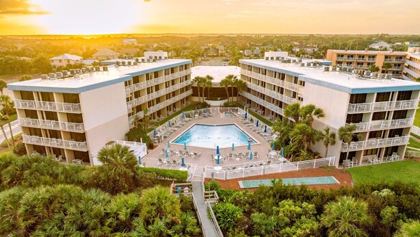 A hotel with a central pool surrounded by multiple balconies, a covered walkway, and lush greenery. - Beach Mode: ON — Garden-Level 1BR Just Steps to the Surf (St. Augustine Beach)