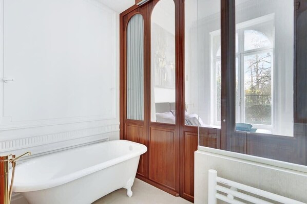 A bathroom with a white bathtub, wooden door, and large windows.