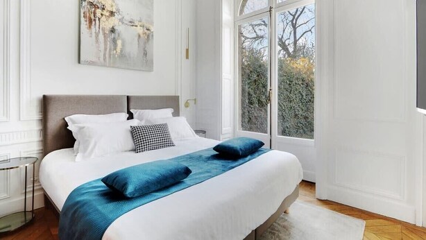 Ein Schlafzimmer mit einem großen Bett, weißen Wänden, einem Fenster mit Blick auf Bäume und einem Bild an der Wand.