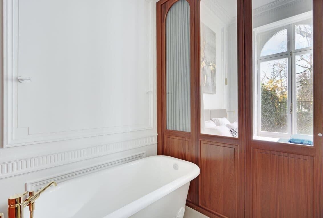 Une salle de bain avec une baignoire blanche, un lambris en bois et une fenêtre donnant sur la forêt.