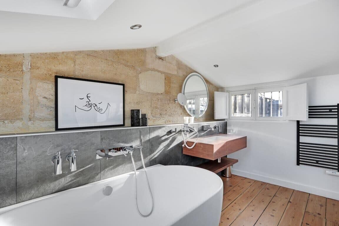 A modern bathroom with a freestanding bathtub, a vanity with a mirror, and a stone accent wall.
