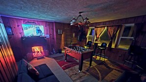 Ein gemütlicher Raum mit einem Kicker, einem Kamin, einem Fernseher und einem Sofa.