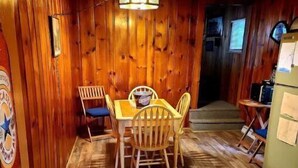Ein Zimmer mit Holzwänden, einem Esstisch und Stühlen, einer Deckenleuchte und einem Kühlschrank.