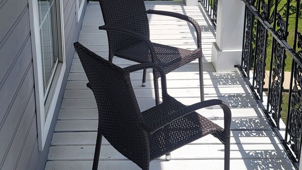 A covered porch with two wicker chairs, white railings, and a view of a green lawn. - It's Five O'Clock off South Lamar (Oxford)