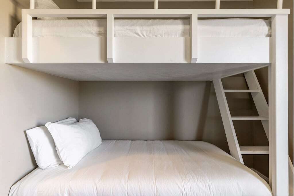 Ein Stockbett mit einer Leiter, weißer Bettwäsche und einer schlichten Wand.