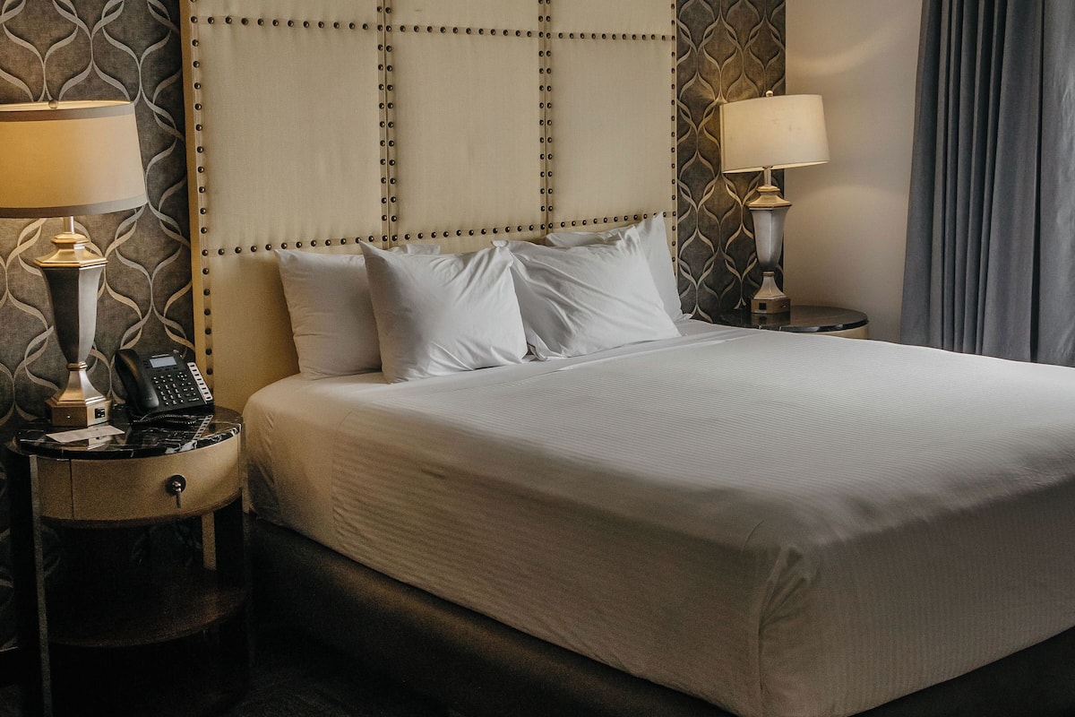 Une chambre d’hôtel avec un grand lit, deux tables de chevet avec des lampes, un mur à motifs et un plancher en bois foncé.