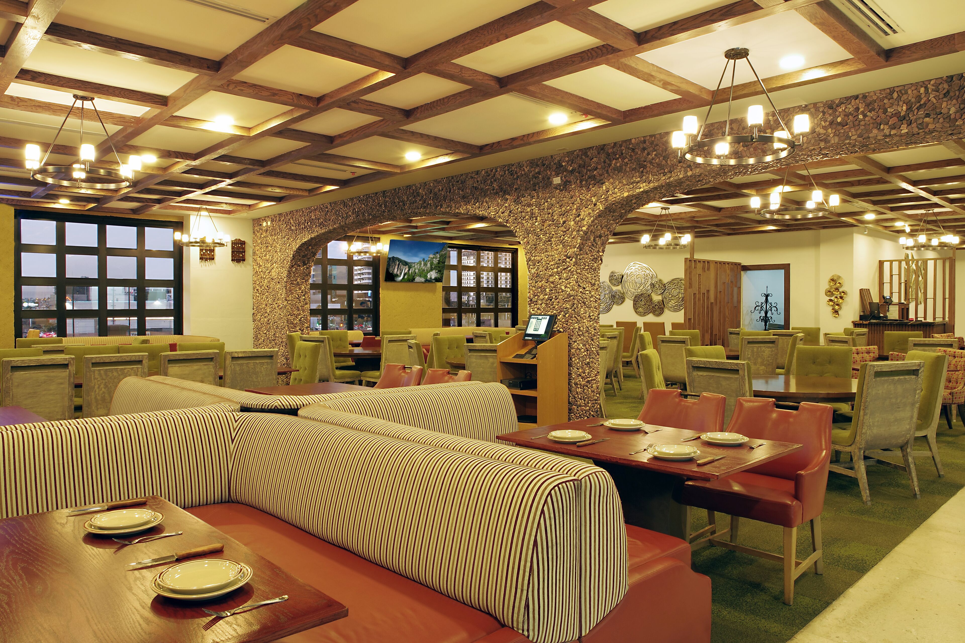 Un restaurant avec de hauts plafonds, des poutres en bois et un mur en pierre. On y trouve plusieurs tables et chaises, ainsi qu’un grand espace avec un banc rembourré.