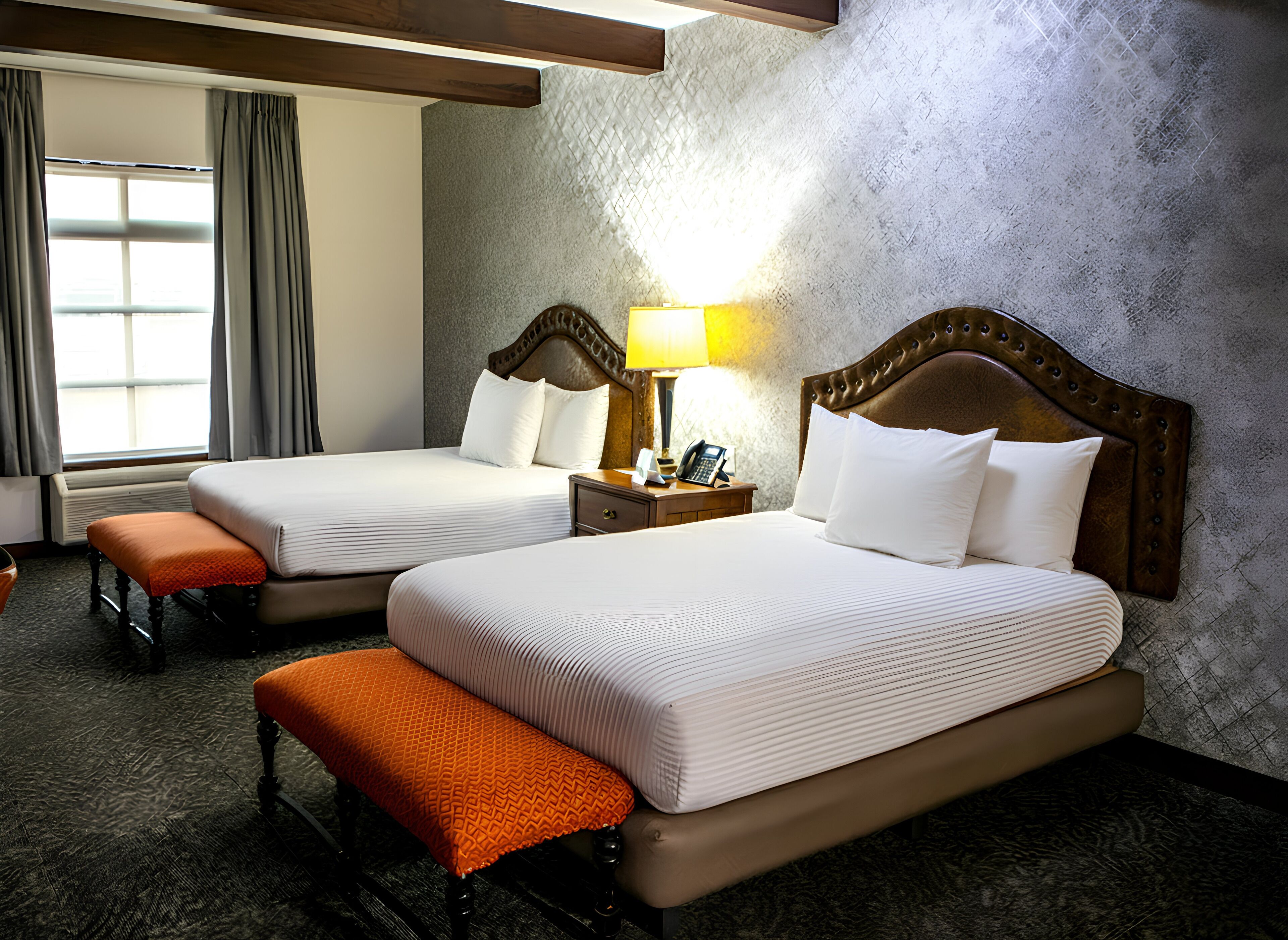 A hotel room with two beds, a bench, a lamp, and a telephone on a nightstand.