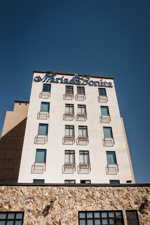 Ein Gebäude mit der Aufschrift "Maria Bonita" auf der Fassade, mit mehreren Balkonen und einer steinernen Fassade im unteren Bereich.