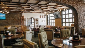 A restaurant with a rustic interior, featuring exposed wooden beams, stone walls, and a variety of seating arrangements. - Hotel María Bonita Chihuahua (Chihuahua)