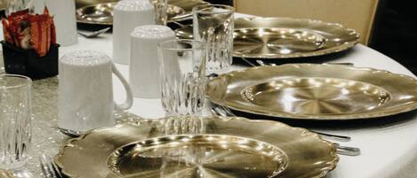 Una mesa servida con platos dorados, cubiertos de plata y vasos transparentes, cubierta con un mantel brillante.