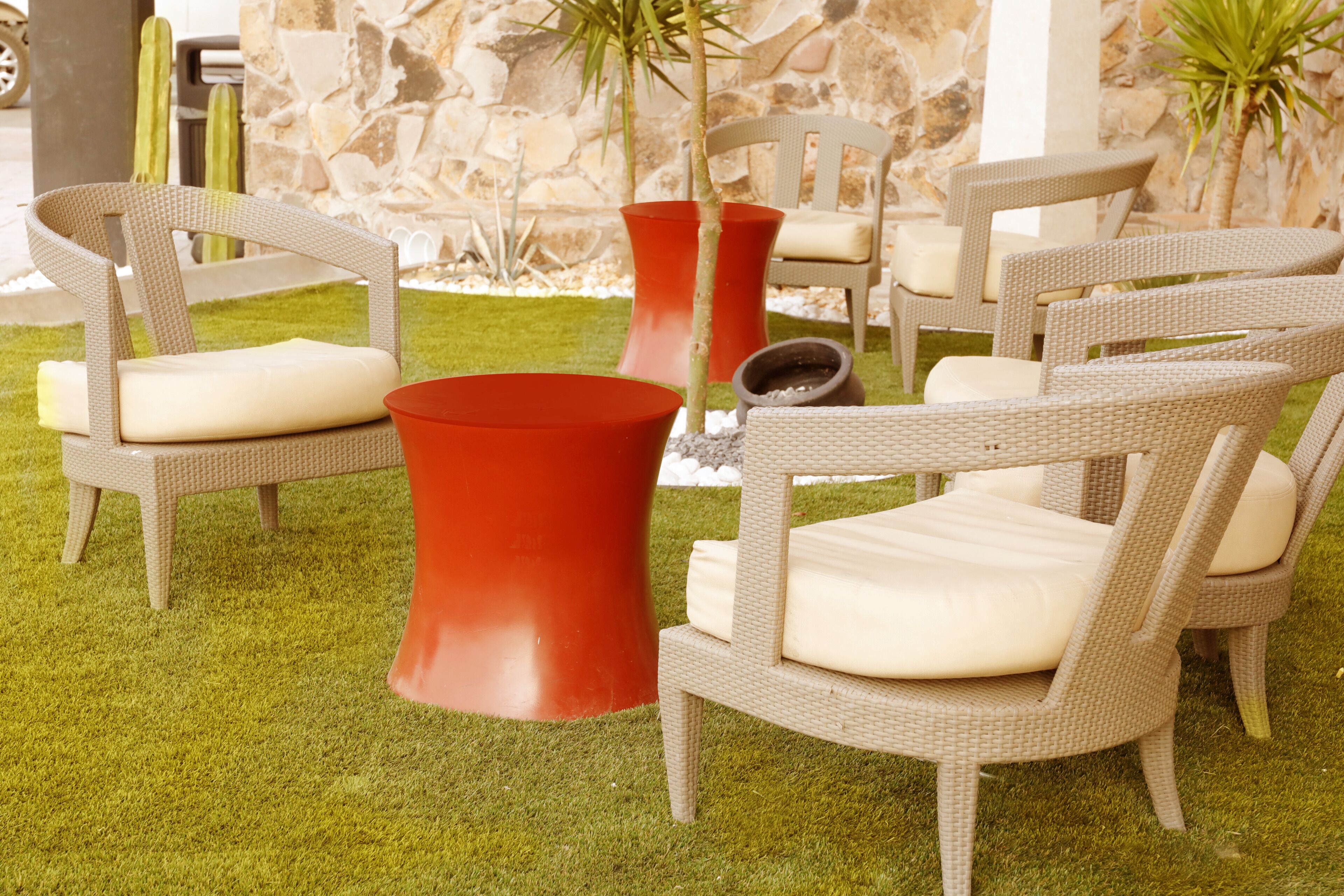 Wicker chairs with cushions, a red planter, and a stone wall in the background.