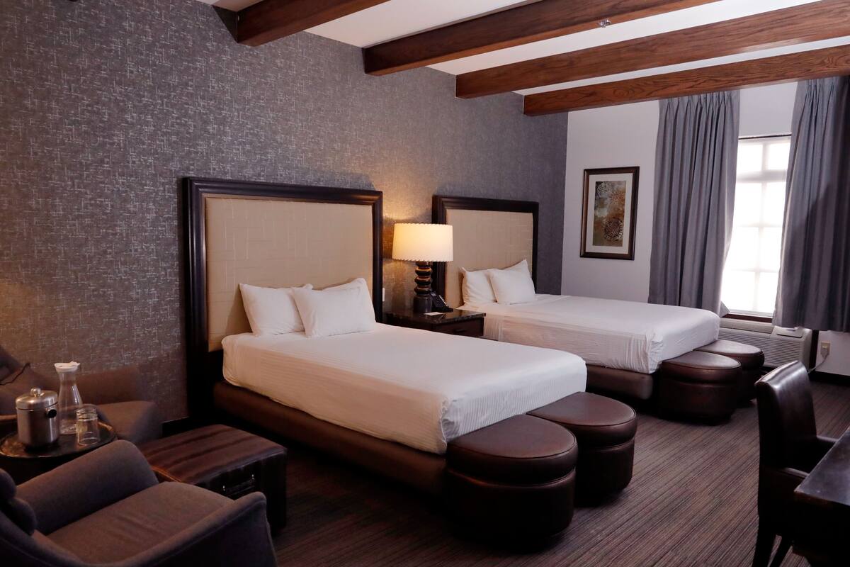 Une chambre d’hôtel avec deux lits, un bureau, une chaise et une petite table avec une lampe.