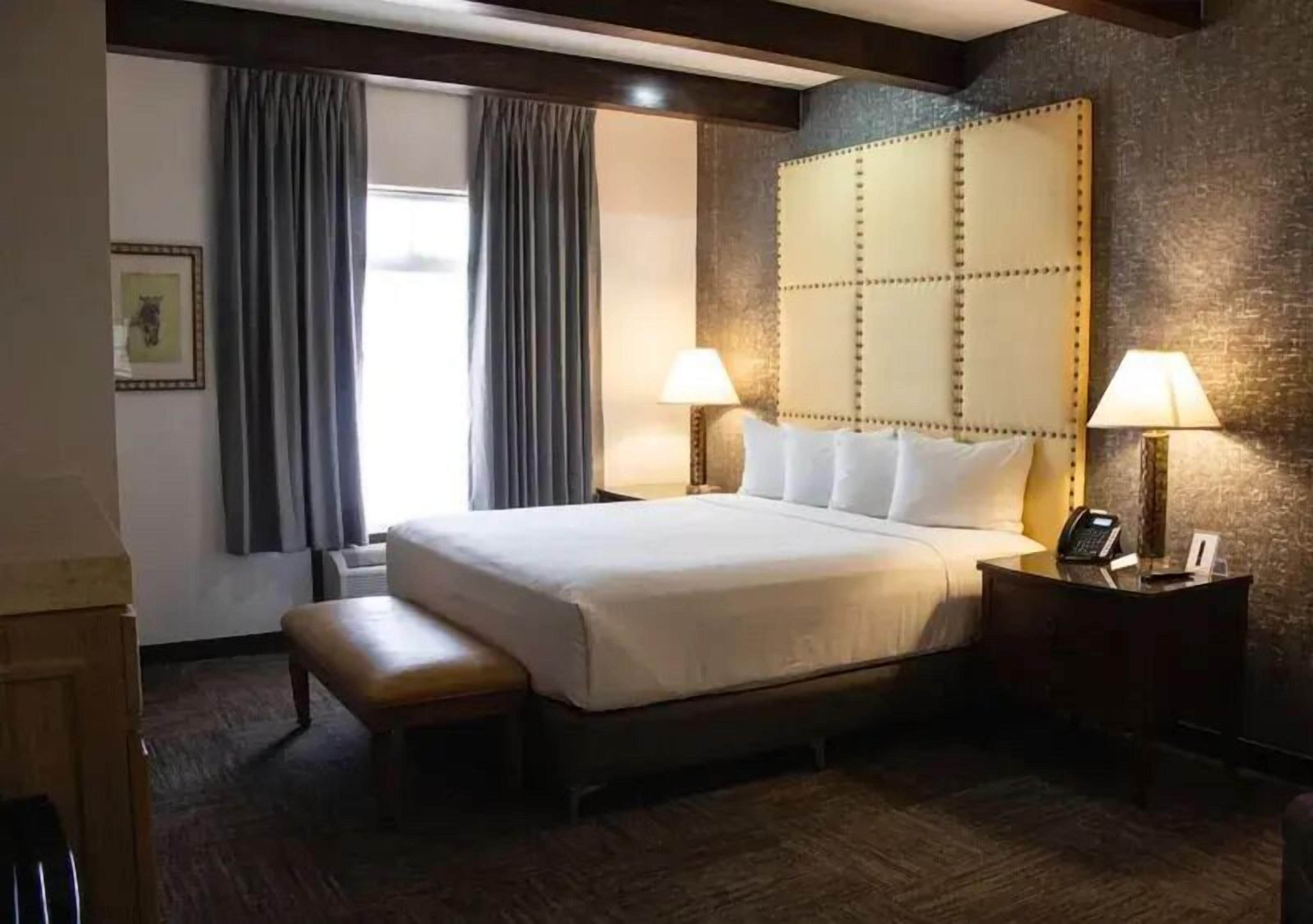 A hotel room with a large bed, two bedside lamps, a wooden bench, a telephone, and a picture on the wall.