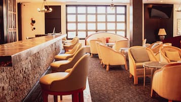 A bar area with a stone counter, multiple bar stools, and a seating area with round tables and chairs.