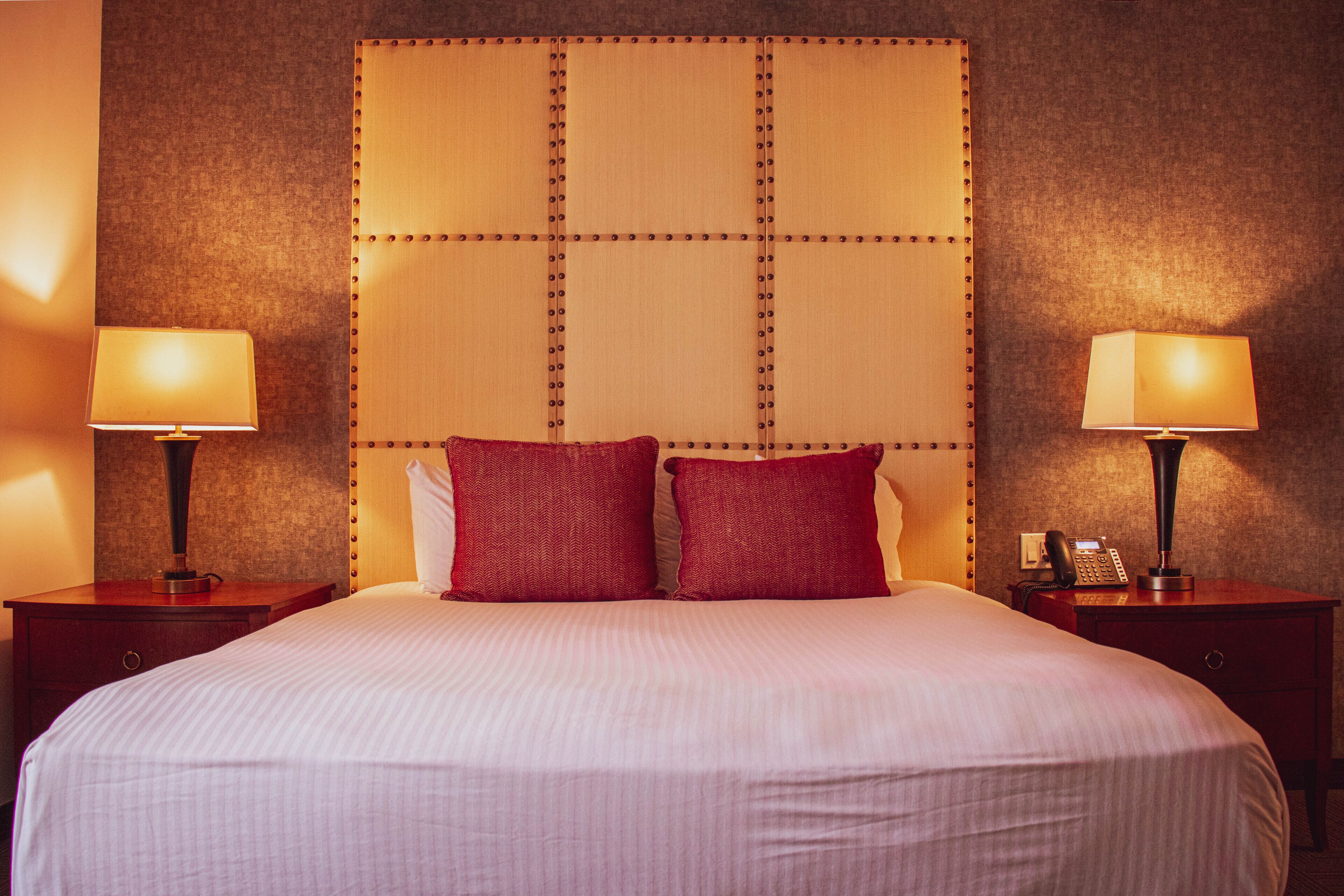 A hotel room with a large bed, two bedside tables with lamps, and a padded headboard.