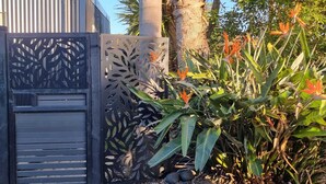 A wooden gate with a decorative metal panel, surrounded by tropical plants and a palm tree. - Luxury  Container House Auckland Airport (Auckland)