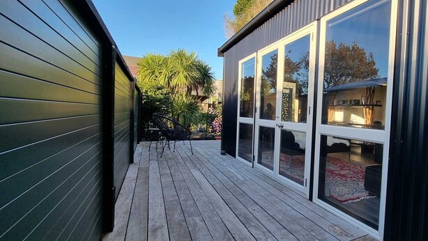 A wooden deck with a glass door leading to a room with a red rug. - Luxury  Container House Auckland Airport (Auckland)
