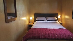 A neatly made bed with a red blanket, two bedside lamps, and a mirror on the wall. - Luxury  Container House Auckland Airport (Auckland)