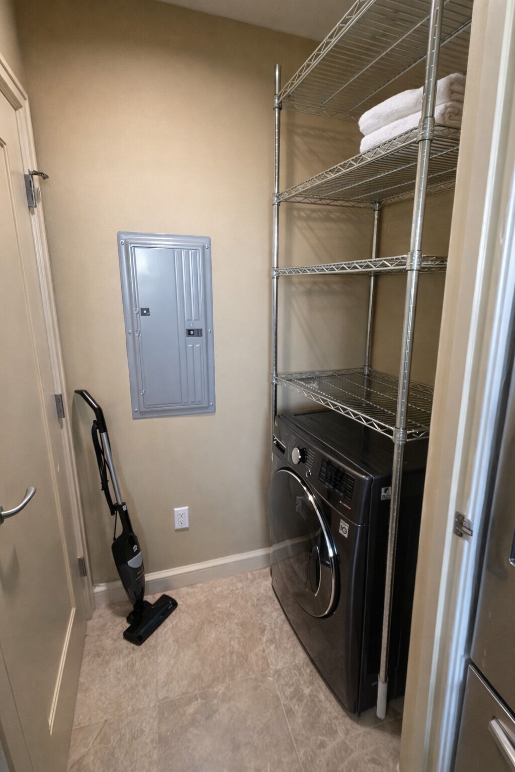 A laundry room with a washing machine, dryer, shelves, and a vacuum cleaner.