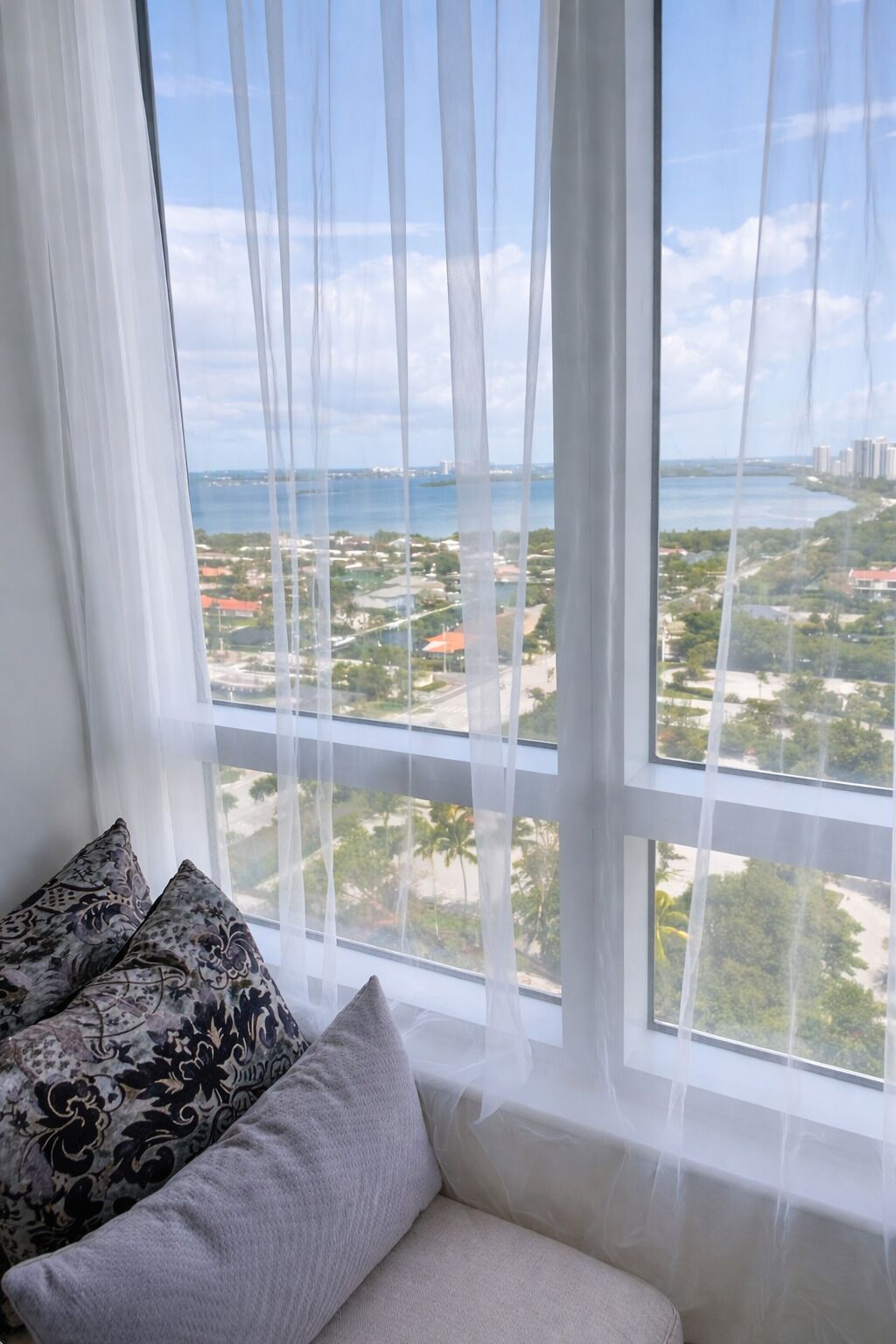 A room with a large window, a sofa, and two patterned pillows.