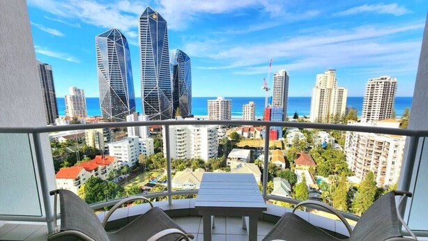 A balcony with a table and chairs, overlooking a cityscape with tall buildings and a clear sky.