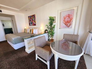 A room with a bed, a sofa, a chair, a table, a potted plant, and artwork on the walls.