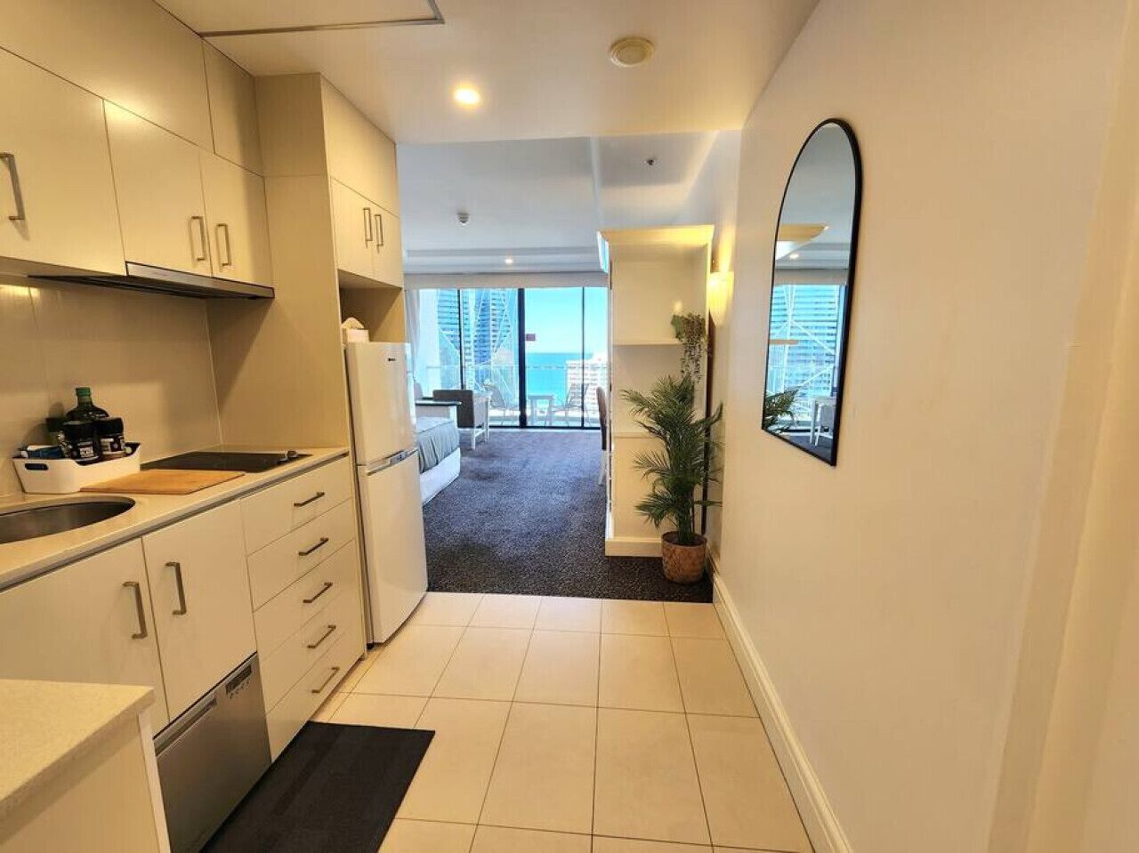 A modern kitchen with white cabinets, a built-in oven, and a large window overlooking a balcony.