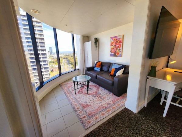 A modern living room with a sofa, coffee table, and a large window offering a city view.