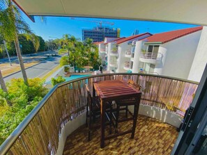 A balcony with a wooden table and chairs, a view of a street with palm trees, and a building under construction in the background.