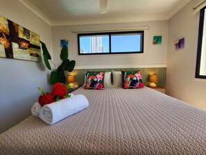 A hotel room with a large bed, a window with a city view, a painting on the wall, and a plant.