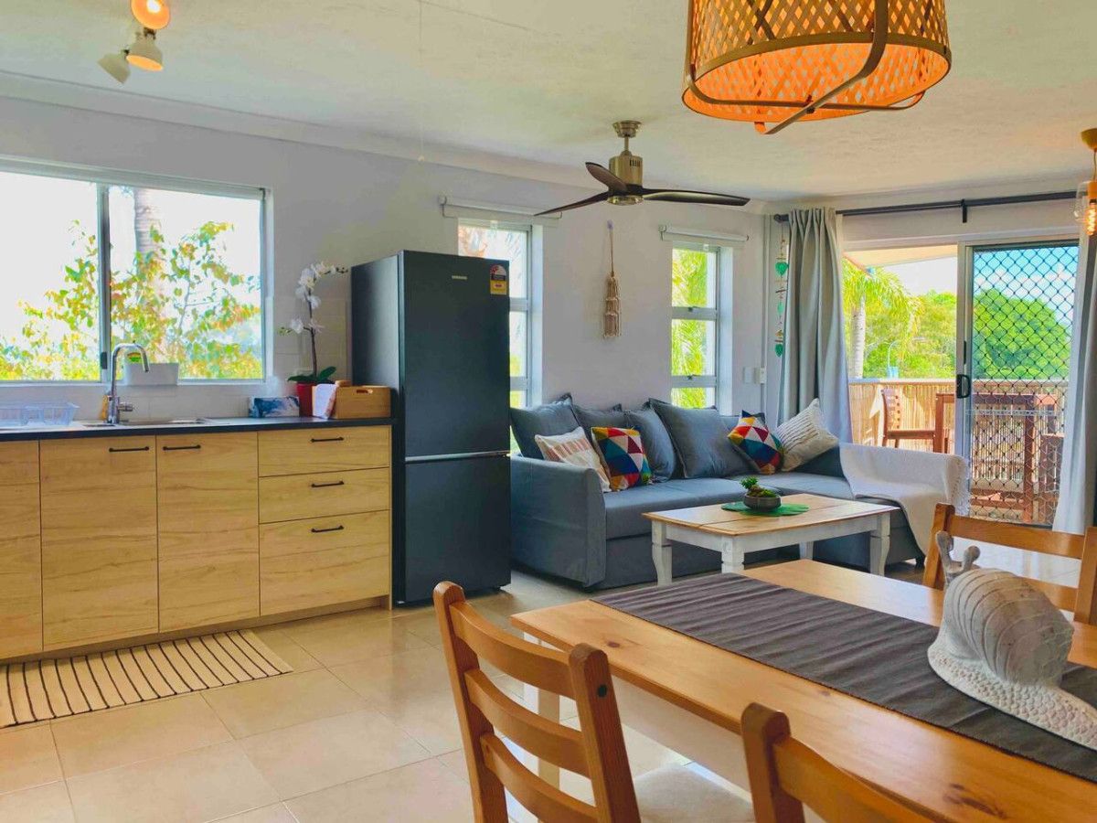 A modern kitchen with a refrigerator, wooden cabinets, and a dining area with a table and chairs.