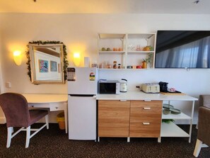 Una kitchenette compacta con microondas, tostadora y armarios, un escritorio con silla y un televisor montado en la pared.