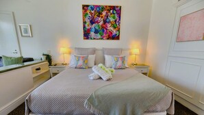 A neatly made bed with a quilted cover, two bedside lamps, and a colorful abstract painting above it. - Oaks Hotel - Deluxe Studio Apartment - Ocean Views (Surfers Paradise)