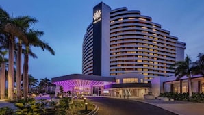 A modern hotel with a curved facade, multiple floors, and a prominent entrance with illuminated signage. - Oaks Hotel - Deluxe Studio Apartment - Ocean Views (Surfers Paradise)