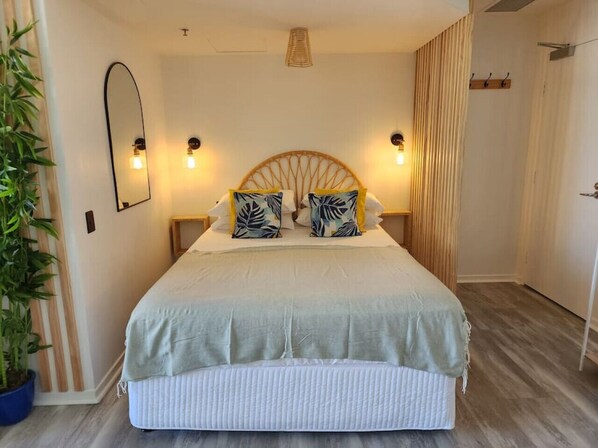 Relax in this serene bedroom featuring a large bed with a rattan headboard, wall-mounted lamps, and a potted plant.