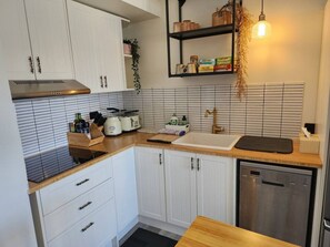 A compact kitchen with white cabinets, a stainless steel dishwasher, and a wooden countertop.