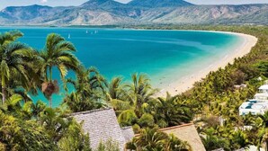 A beach with clear turquoise waters, palm trees, and a mountainous backdrop.