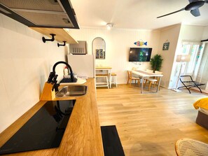 A modern kitchen with a black countertop, stainless steel sink, and a wooden backsplash. There is a dining area with a table and chairs, and a TV mounted on the wall. - [Holiday Apartment] In Ramada Resort- Port Douglas (Port Douglas)