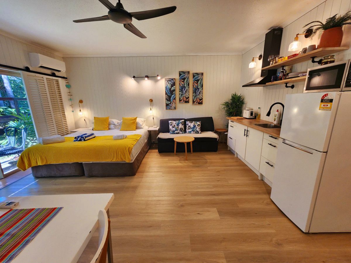A compact living space with a bed, sofa, dining table, kitchenette, and a ceiling fan.