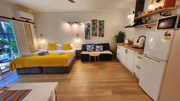 A compact living space with a bed, sofa, dining table, kitchenette, and a ceiling fan.