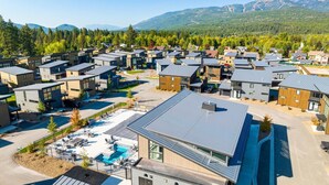 A modern residential complex with multiple two-story houses, a central swimming pool, and a mountainous backdrop. - Glacier State of Mind (Whitefish)